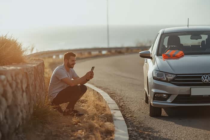 Tourist photographing minor rental car bumper damage on a Greek coastal road